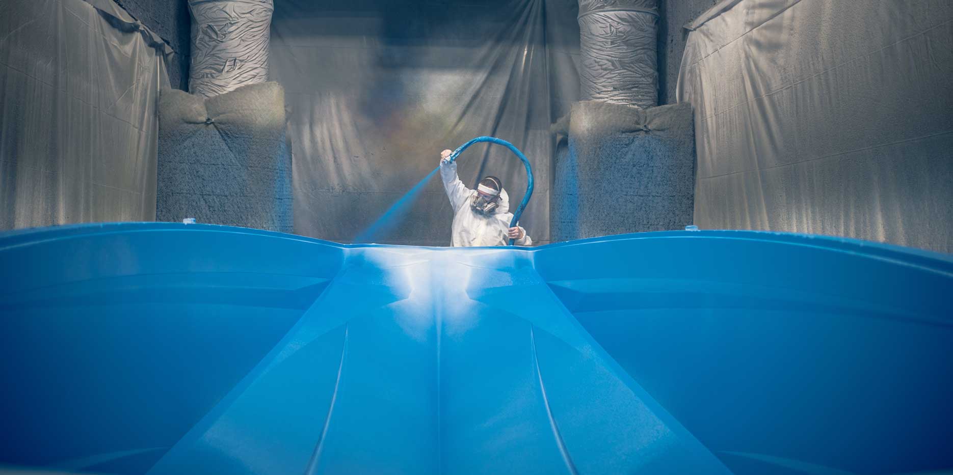Worker spraying a hull with blue paint.