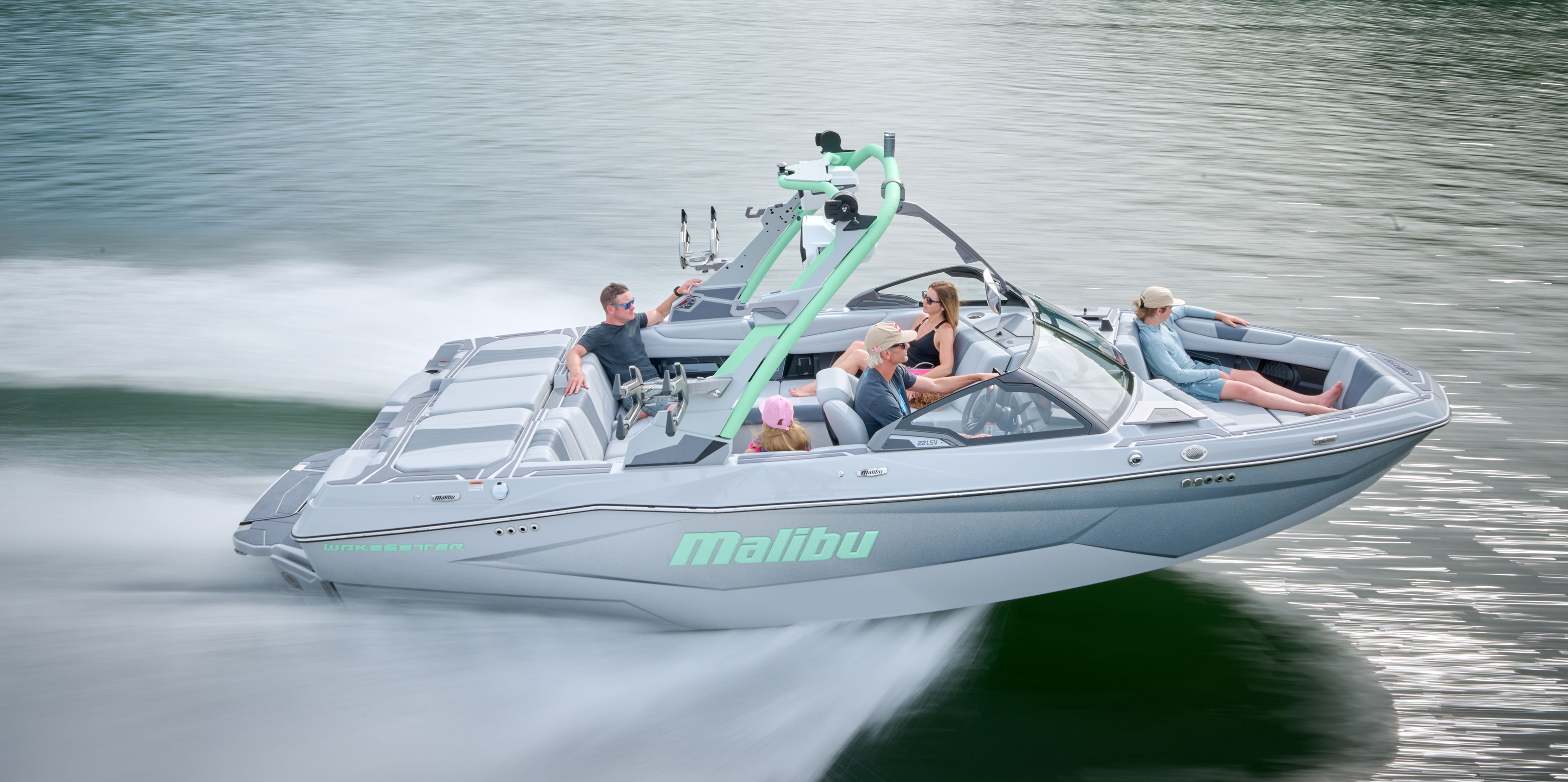 Side profile of the 2026 Malibu Wakesetter 22 LSV gliding across a calm lake with a rider behind the boat.