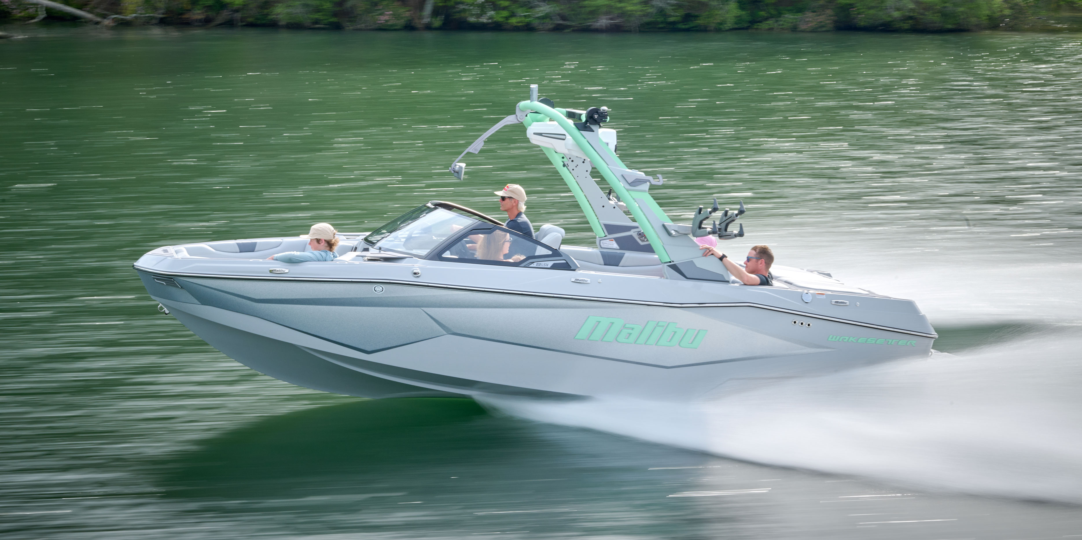 Wakesurfer riding a clean wave behind the Malibu Wakesetter 22 LSV, with onlookers watching from the rear lounge.