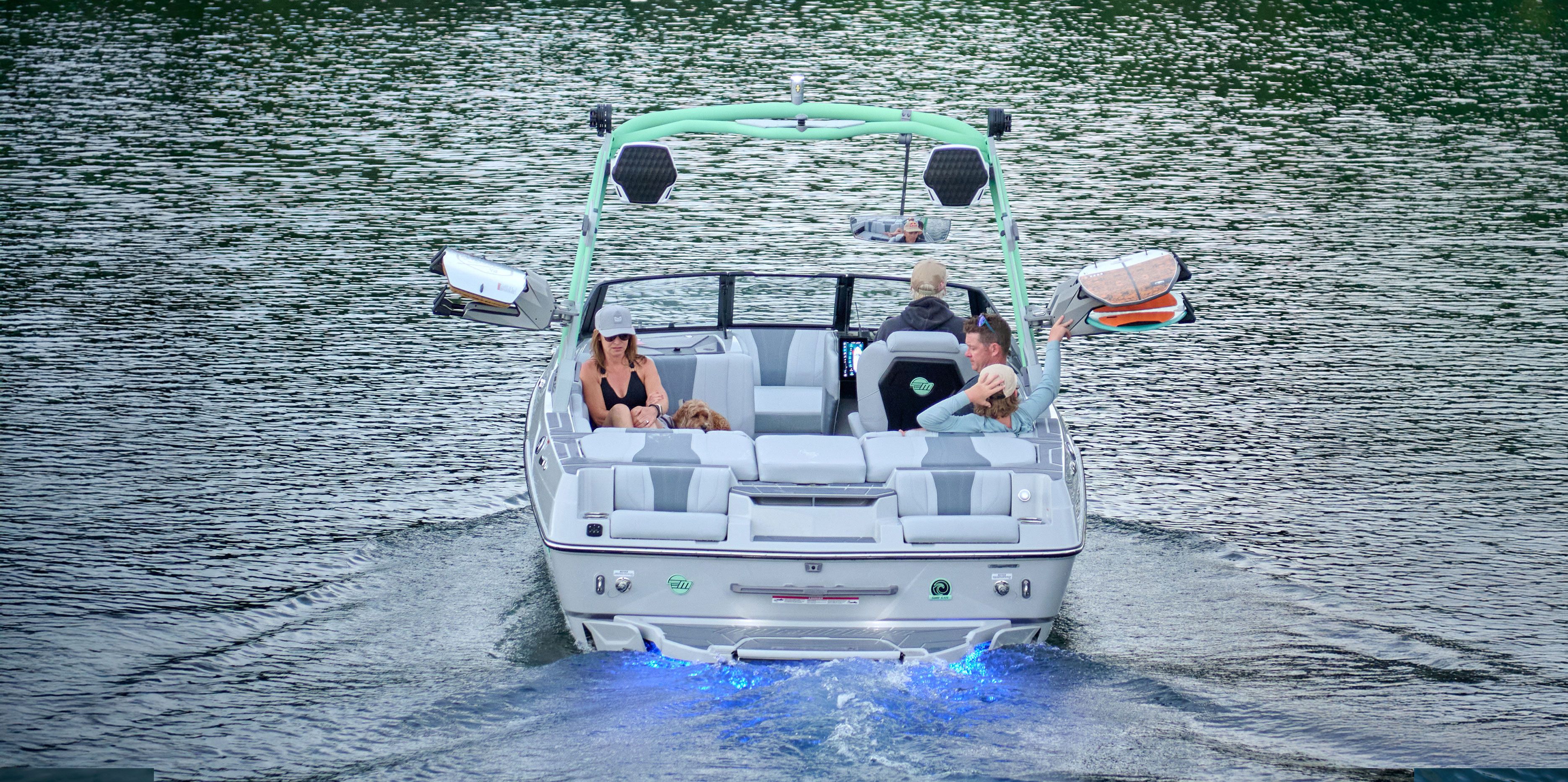 A wakesurfer rides close behind the Malibu Wakesetter 22 LSV while passengers relax and watch from the rear lounge.