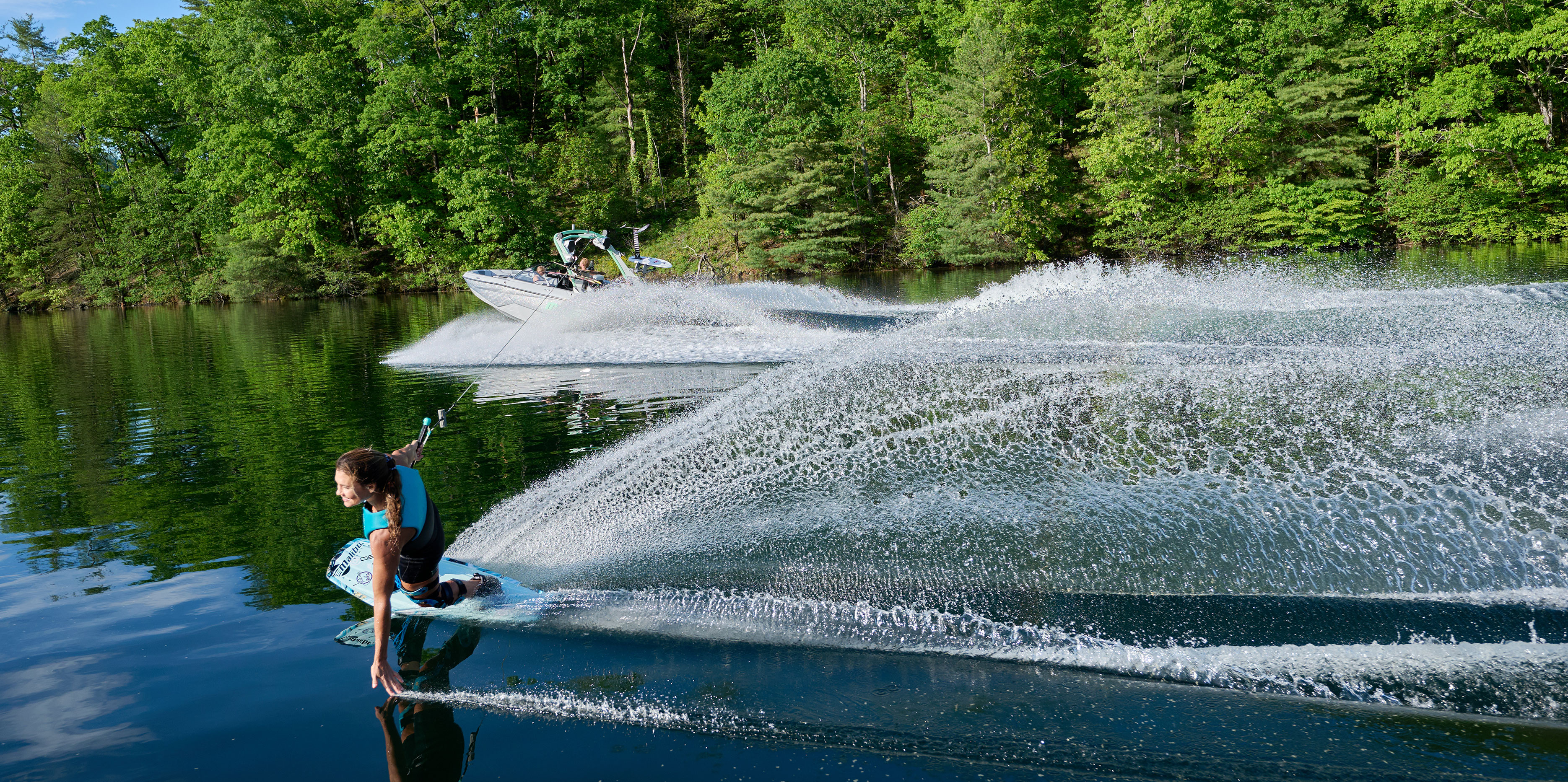 Surfer riding a tall, well-formed wave behind the Malibu Wakesetter 22 LSV with clean water conditions.