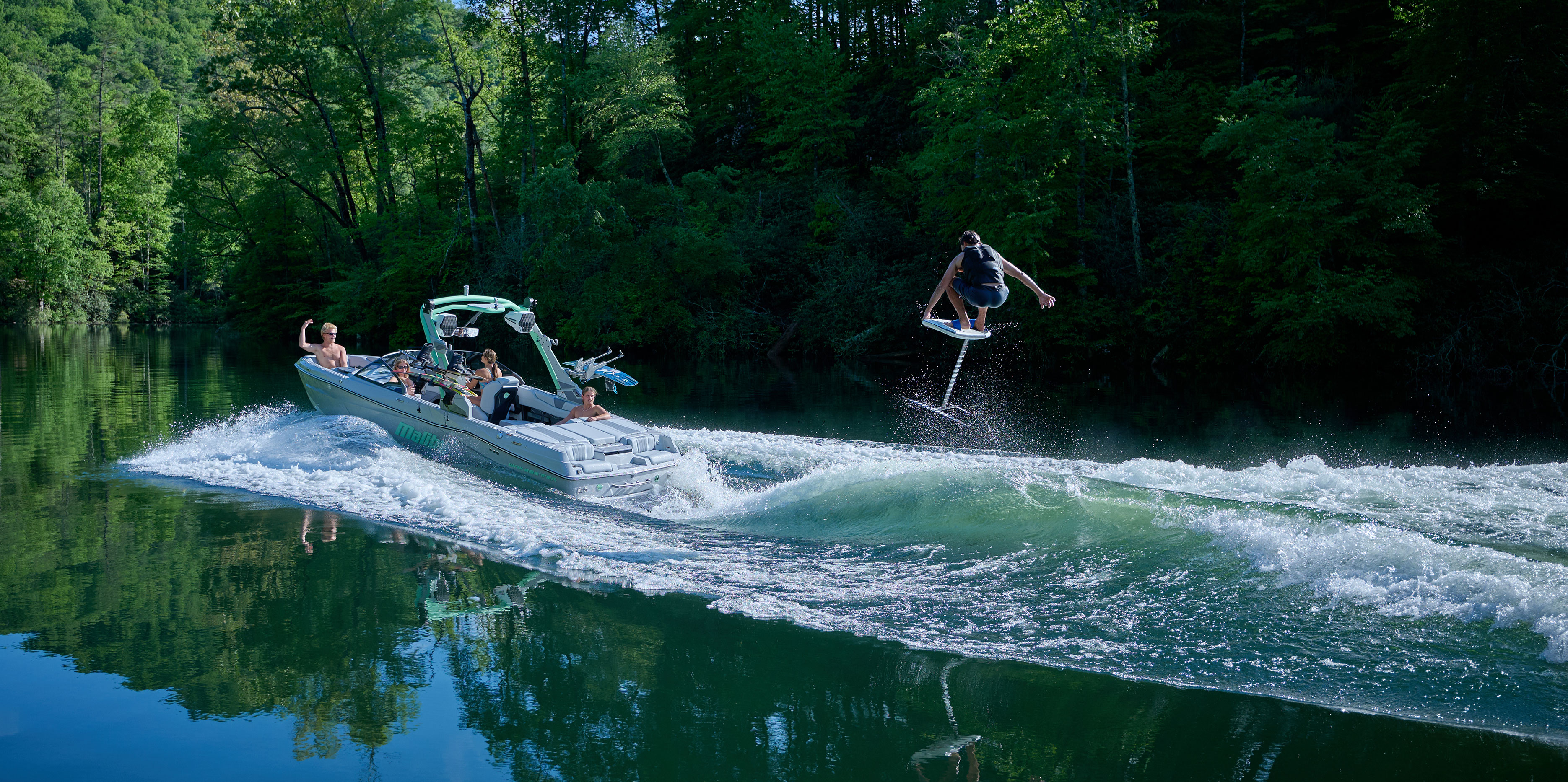 Wakesurfer rides a well-shaped wave behind the Malibu Wakesetter 22 LSV with passengers watching from the transom.