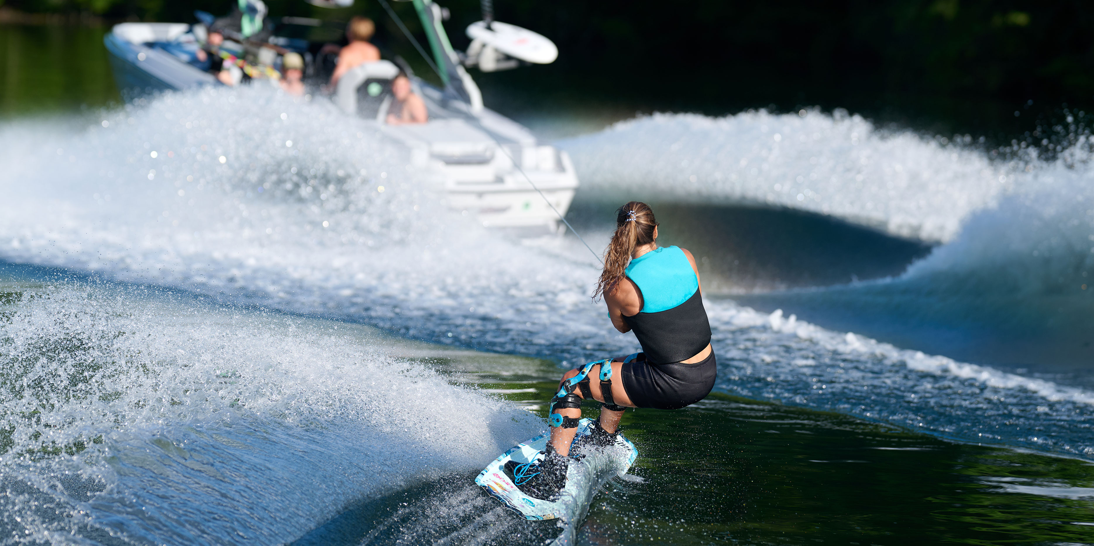 A surfer cuts across a smooth, well-shaped wave behind the Malibu Wakesetter 22 LSV in golden hour light.